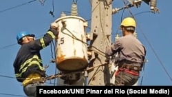 Dos trabajadores de la UNE de Pinar del Río están trabajando en un poste.